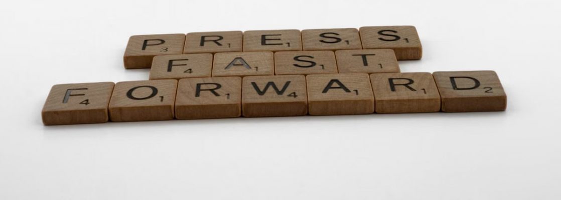 A motivational phrase 'Press Fast Forward' spelled with Scrabble pieces on a white background.